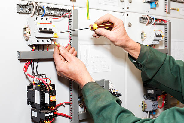 Electrician working in electrical shield with an electric screwdriver.